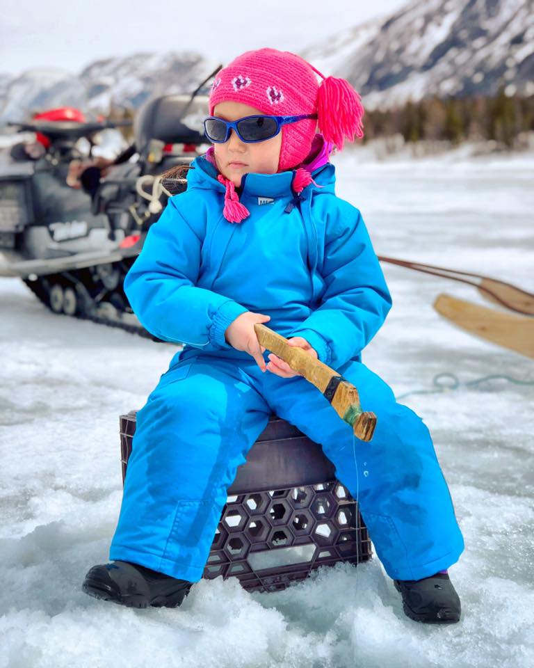 young girl sitting in a snow suit ice fishing
