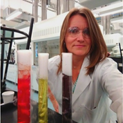 Laura Ingram in the lab behind cylinders with different coloured solutions