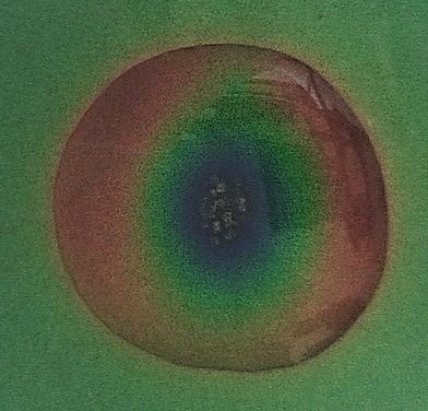 a thermochromic plastic appearing greenish with water puddle which appears red outer ring, then yellow, green and then a very dark blue centre – looks like a mood ring.