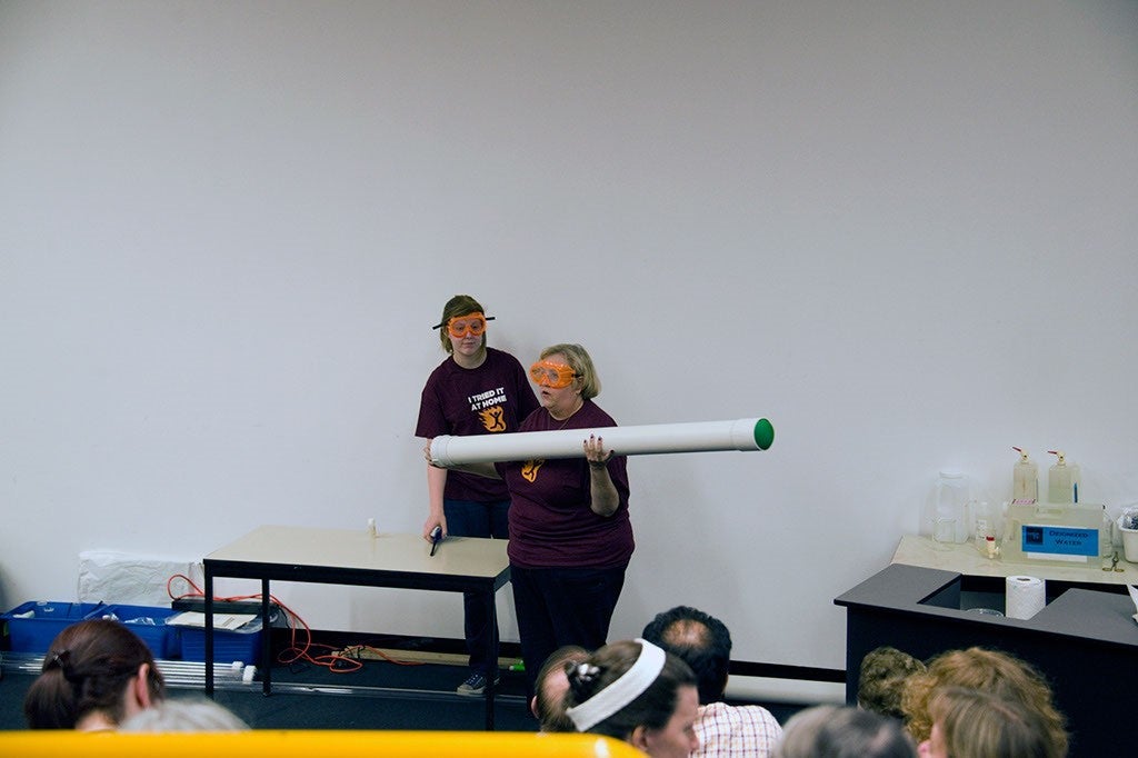 Kathleen Holley holding a large white tube as part of a ChemEd demonstration.