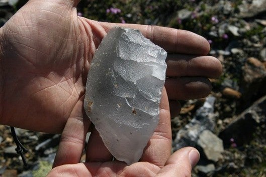 a hand holding a piece of off-white quartz into a sharp-edge tool