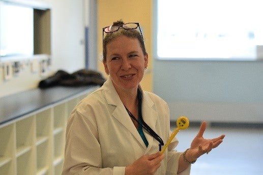 Sue Stathopulos in a lab coat holding a yellow thermometer