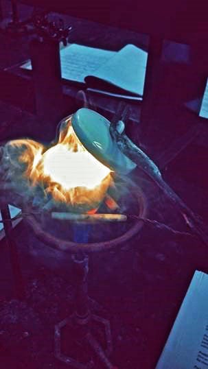 glowing and &quot;smoking&quot; material in a crucible over a lit Bunsen burner. Tongs are lifting the lid