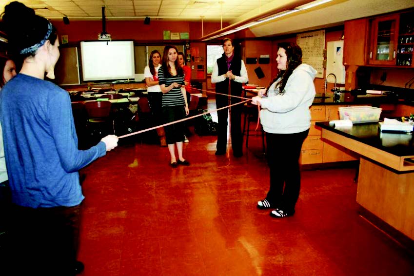 three  students -- two pulling on the ends of a stretching tube with one pulling from the middle demonstrating a water molecule