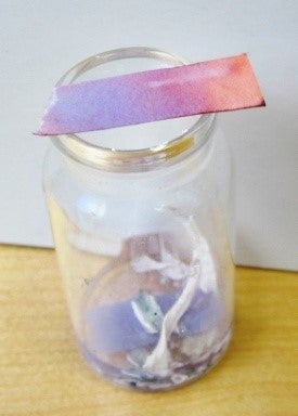 A piece of red litmus paper which appears to have turned blue placed over the top of a jar with pieces of white material on the jar’s bottom.