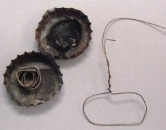 Two bottle blackened bottle caps, one with a strip of coiled magnesium ribbon and the other is empty. Also pictured is a wire with a loop made on one end – the loop is the size of a bottle cap.