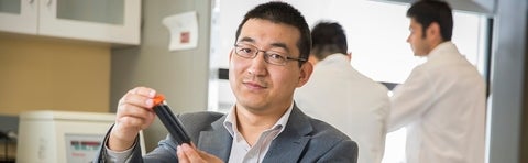 a man with glasses and black hair holding a test tube