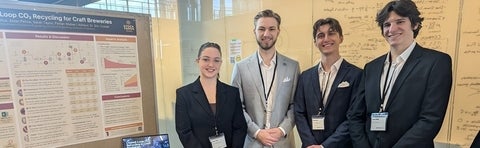 a woman and three men standing beside a poster board