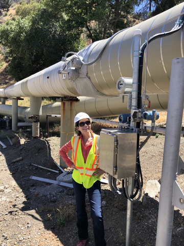 Rosemary Niechcial in a yellow vest sunglasses and hard hat standing by silver pipes