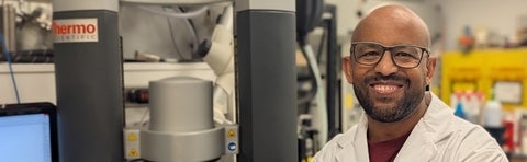 a man smiling wearing glasses and a lab coat