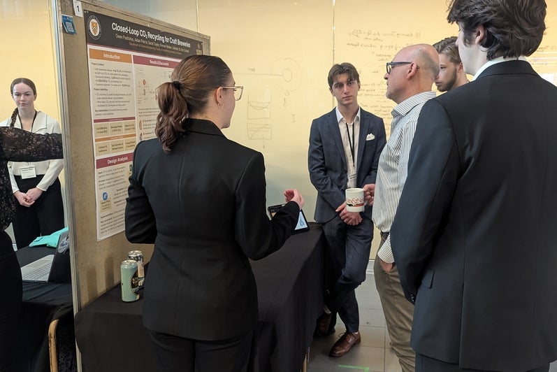 a man looking at a poster board with three men and a woman looking on