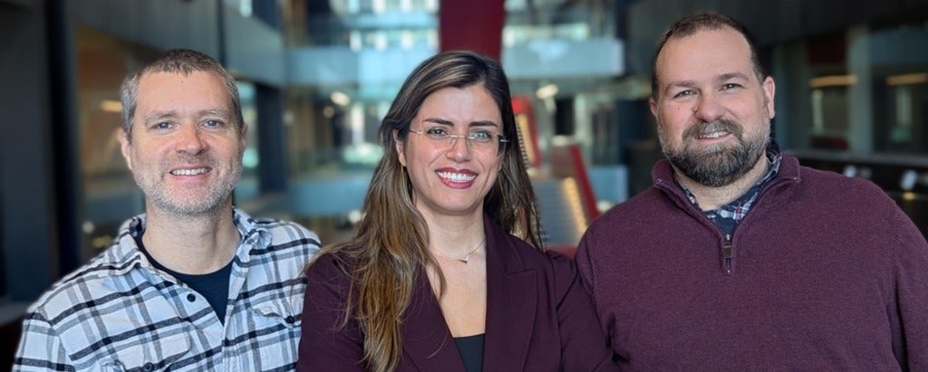 two men smiling with a woman with long hair and glasses in the middle