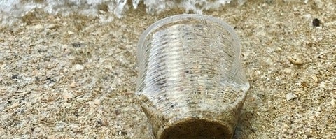 a plastic cup lying on the beach filled with sand and water