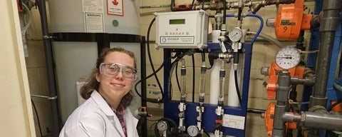 a young woman in safety glasses smiling in front of equipment