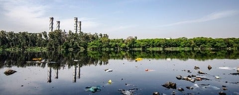 a body of water with platic pollution floating in the water smoke stacks and trees in the background