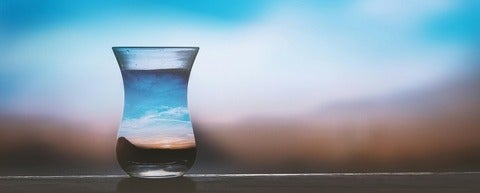 a glass filled with water reflecting the sky, sun and earth