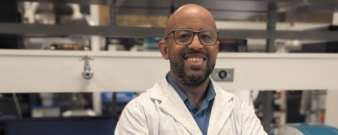 a man with glasses smiling in a white lab coat