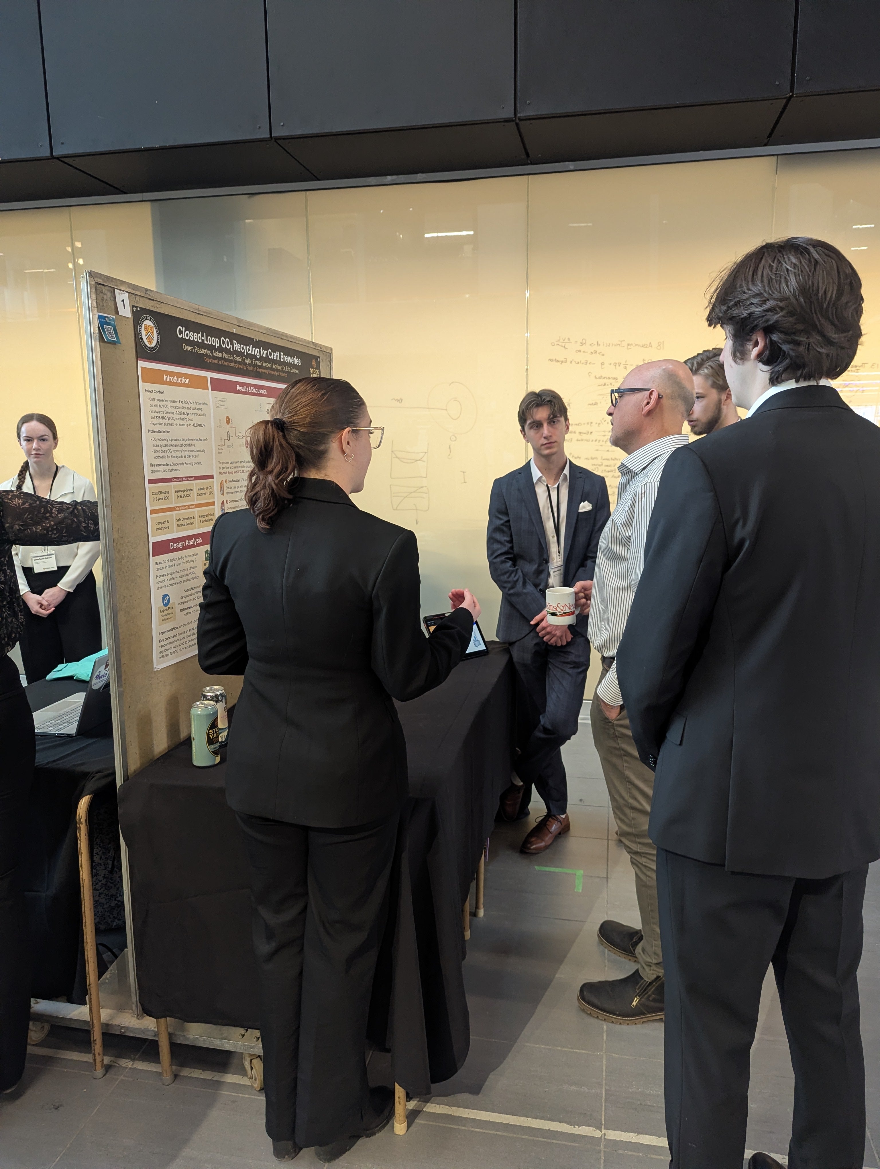 a man looking at a poster board with three men and a woman looking on