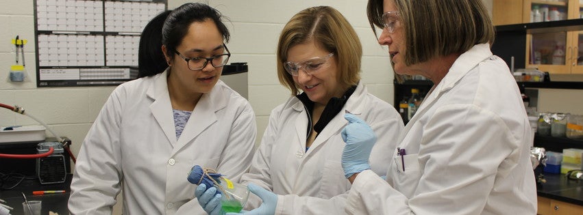 Three lab workers looking at a beaker