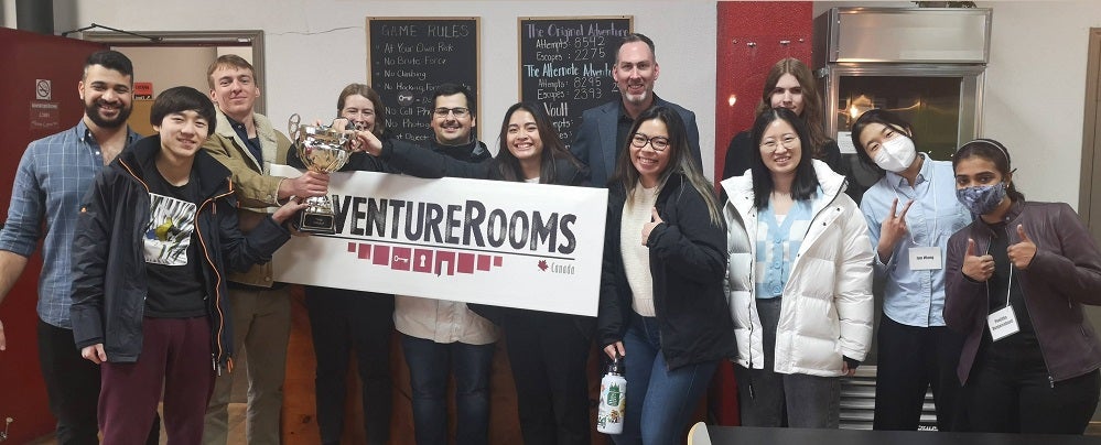 Professor Michael Pope at adventure game room with his students holding a trophy.