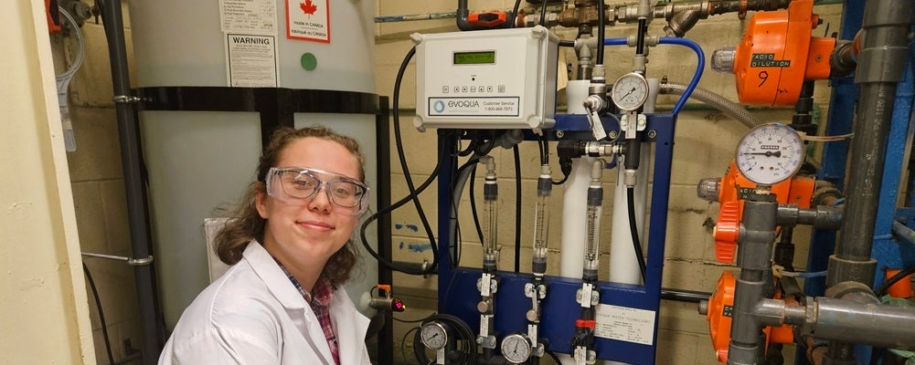 a young woman in safety glasses smiling in front of equipment