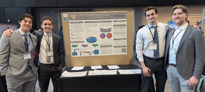 four men smiling beside a poster board
