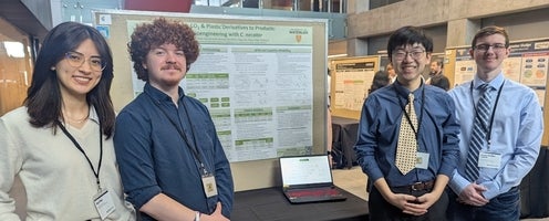 a woman and three men standing beside a poster board