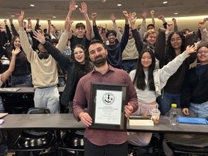 a man standing in front of a group of cheering students holding a plaque