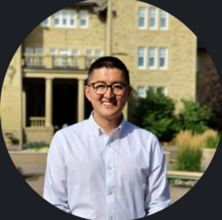 a man with black hair and glasses smiling