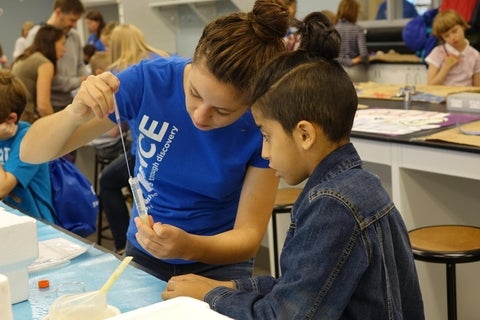 A volunteer shows a kid how to pipette a sample into a test tube.