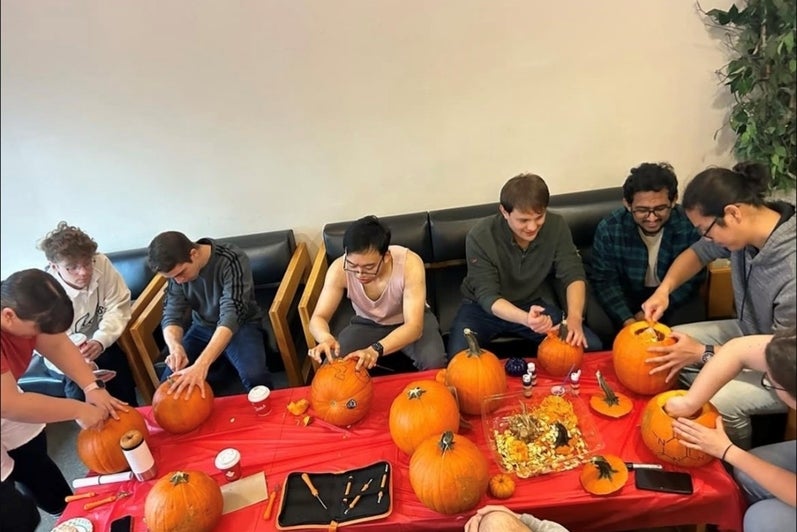 Students enjoying coffee and doughnuts with pumpkins on the table.