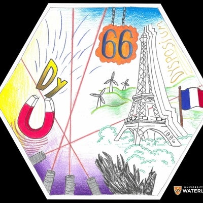 Colored pencil and pen. A large Eiffel tower on the right with a French flag, plus wind turbines in the background. Above the atomic number “66” highlighted in orange. Left is the chemical symbol “Dy” being attracted to a horseshoe magnet. Four laser beams criss-cross the tile. Bottom right, the natural gray form of dysprosium.
