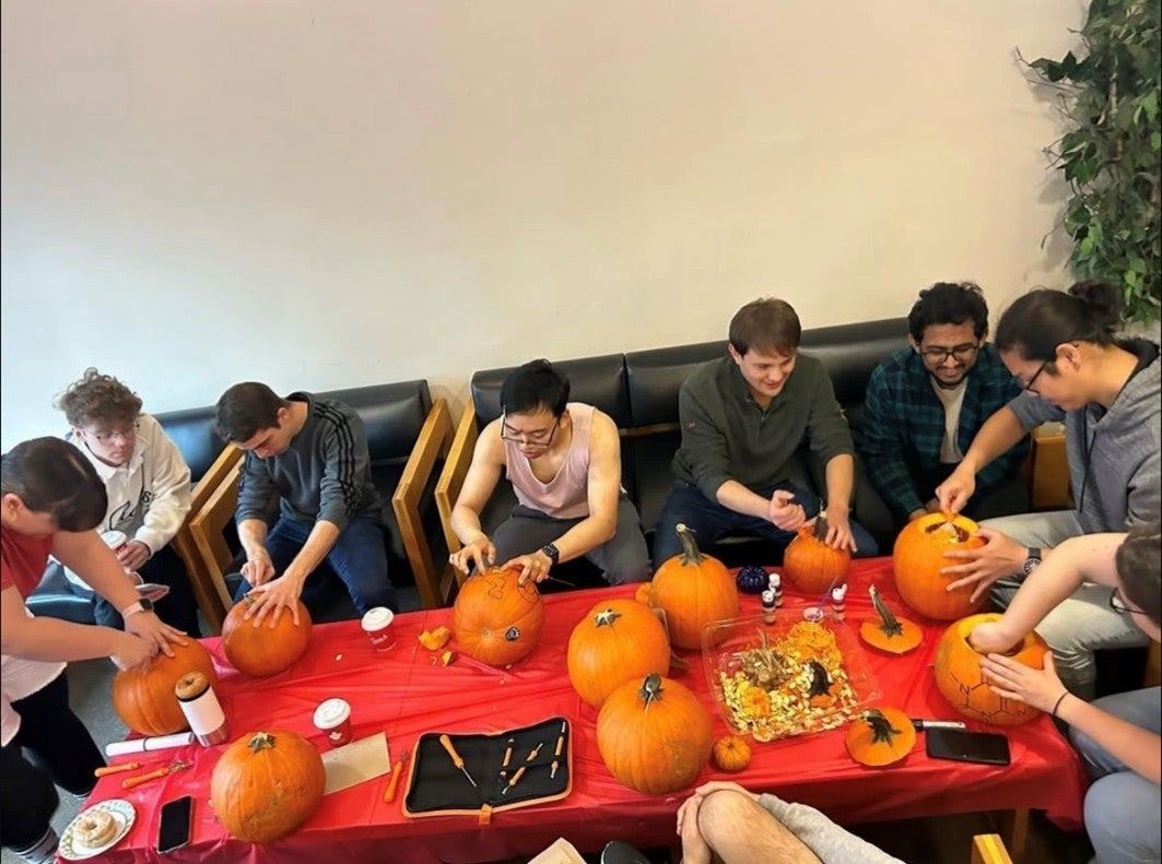 Students enjoying coffee and doughnuts with pumpkins on the table.