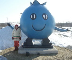 A person standing next to a blueberry mascot in the winter.