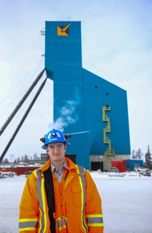 young man dressed in safety jacket, standing in front of large gold mine
