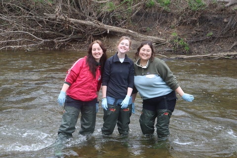 3 girls smiling standing in a river, wearing waders