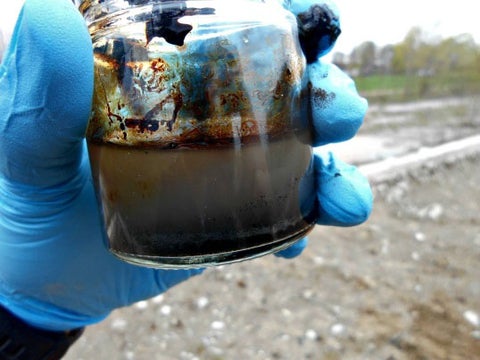 gloved hand holding dirty water in a jar