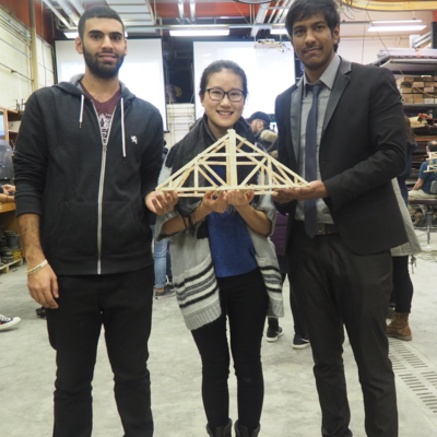 Three students holding a bridge made out of popsicle sticks