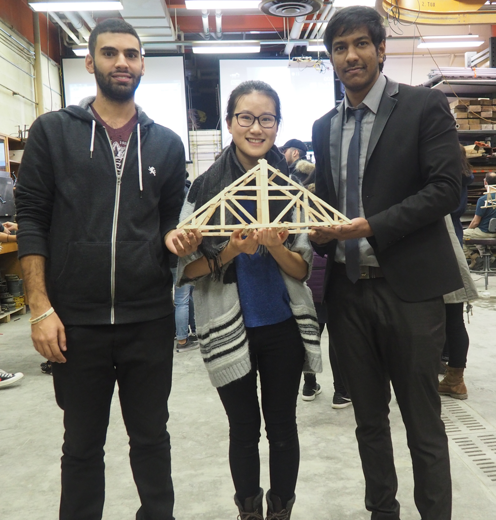 Three students holding a bridge made out of popsicle sticks