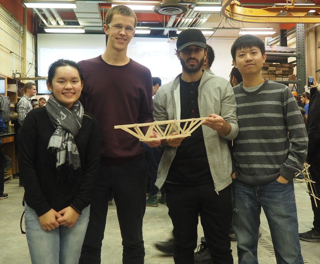 Four students holding a bridge made out of popsicle sticks