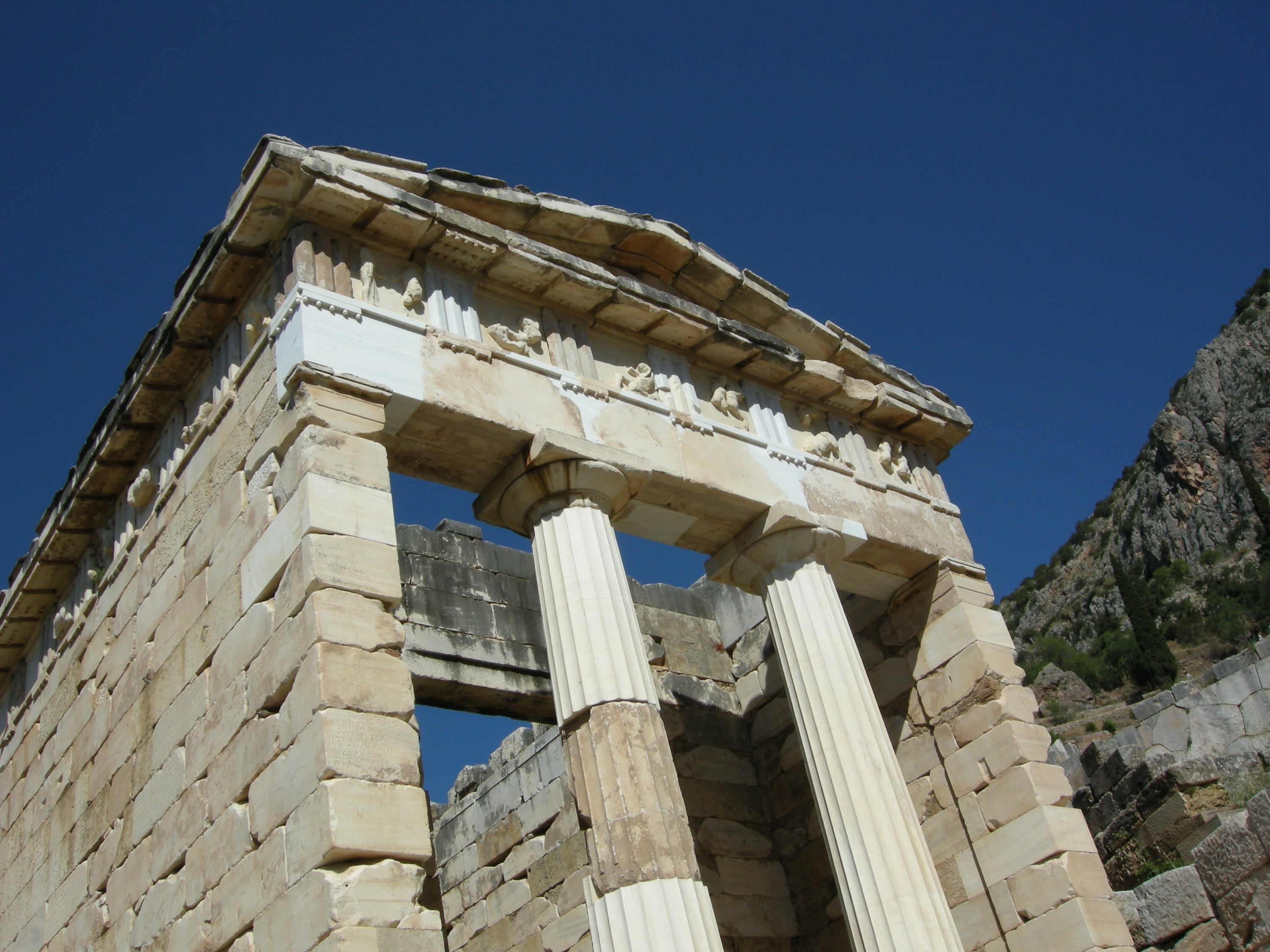 A close of up of the ruins of a Classical era temple showing the front of the building tall columns holding up a sculpted cornice