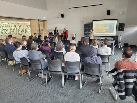 Participants sitting in a gallery seating listening to a slide presentation