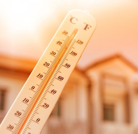 Thermometer showing high temperatures with blurry housing and sky in background