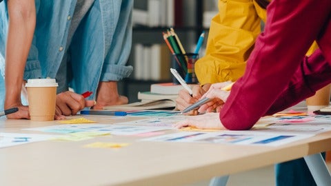 three people's arms at a table designing something with pens