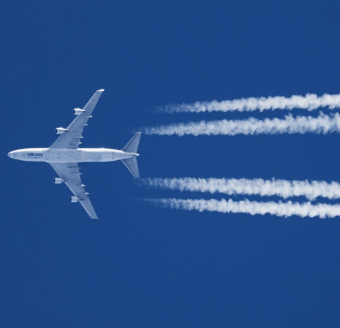 Airplane with contrails in clear blue sky.