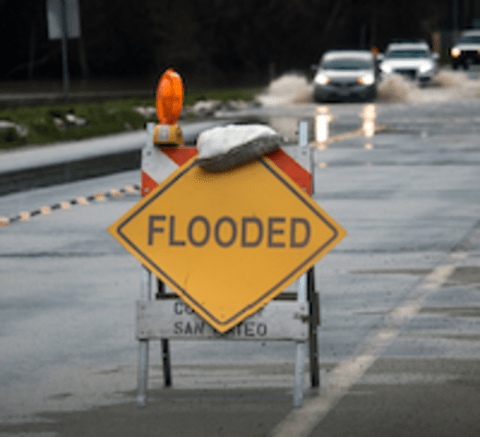 flooded sign on road with flood water and cars
