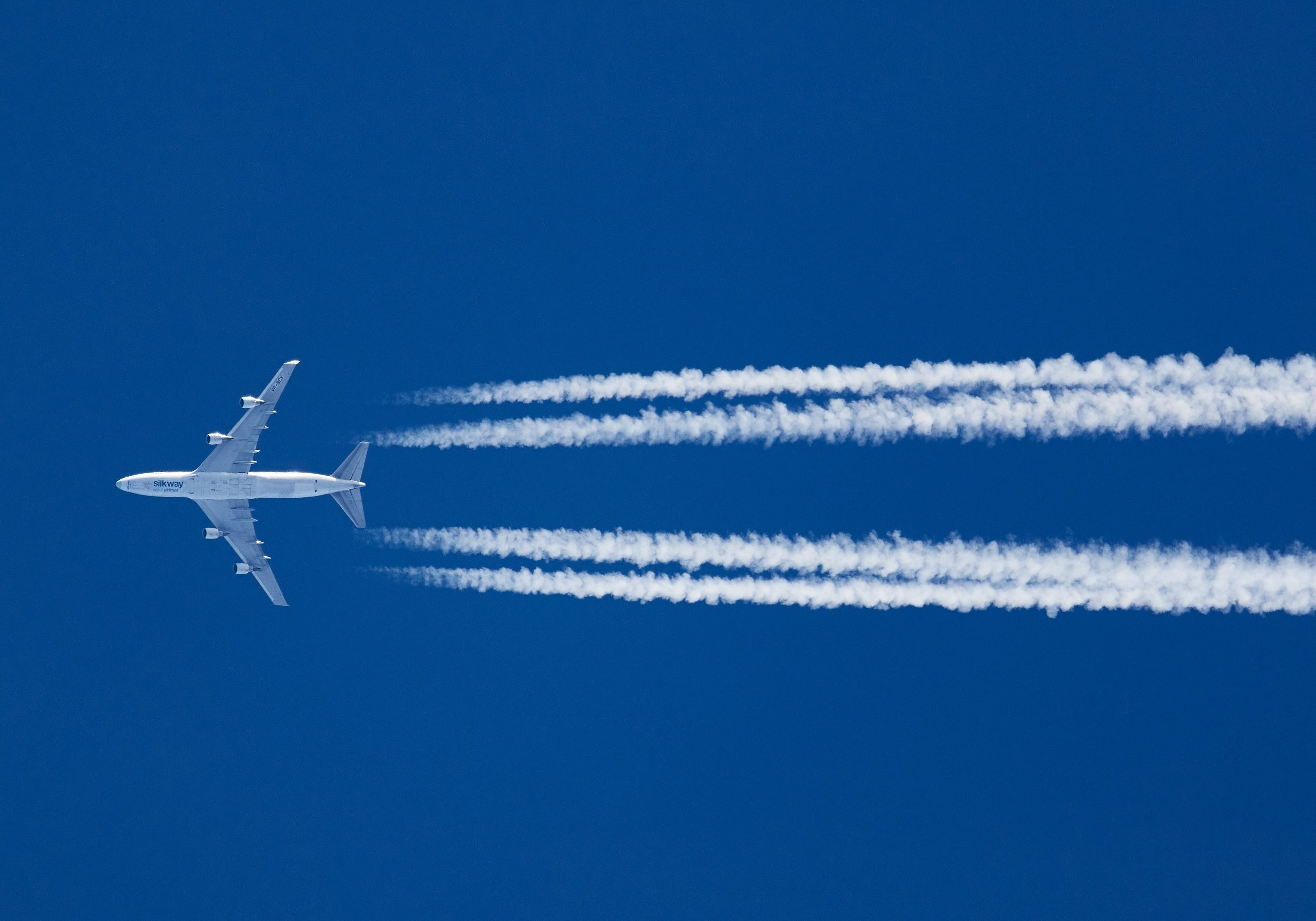 Airplane with contrails in clear blue sky.