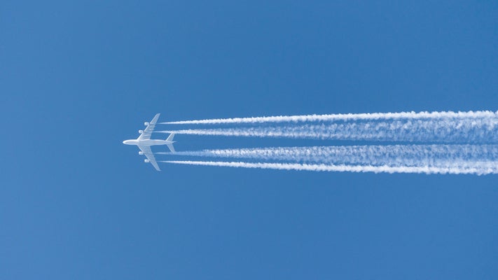Airplane with contrails in clear blue sky.
