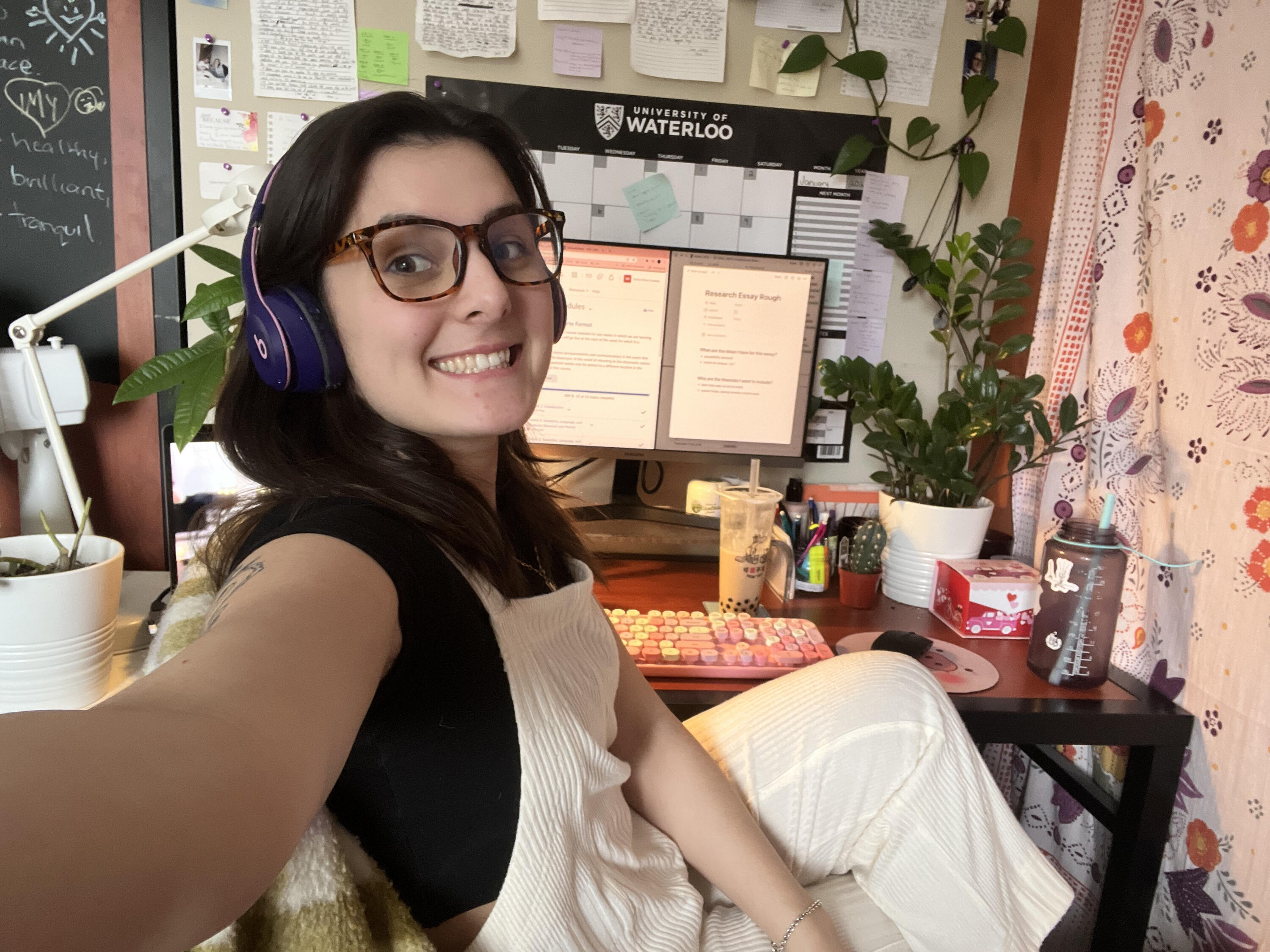 A photo of Sydney sitting at her work desk, smiling and wearing headphones.