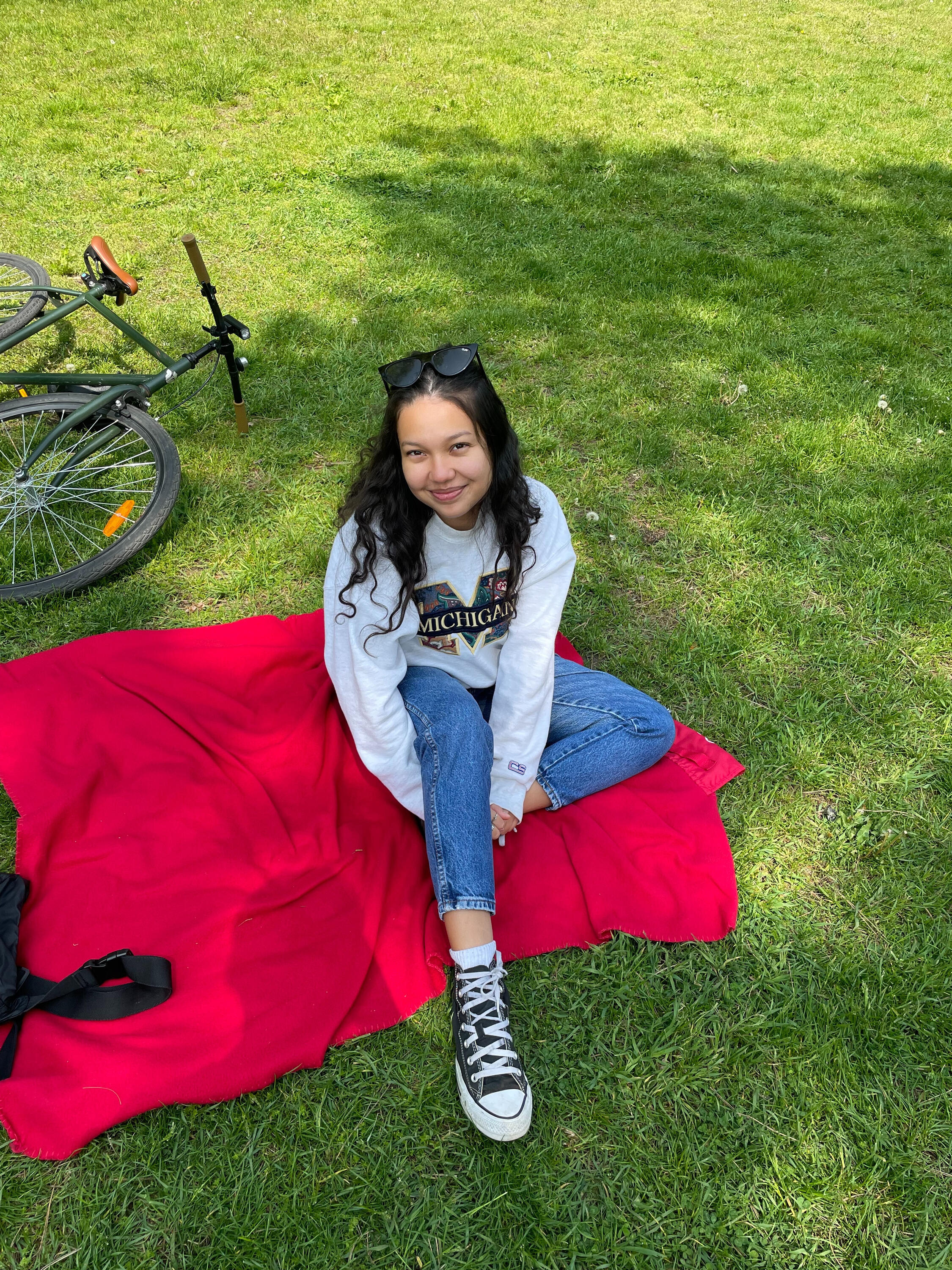 Putri sitting down on a picnic blanket in the grass. 